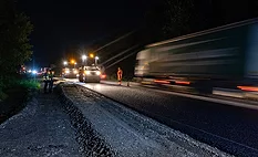 Nighttime highway work zone with workers and passing traffic under active construction conditions.