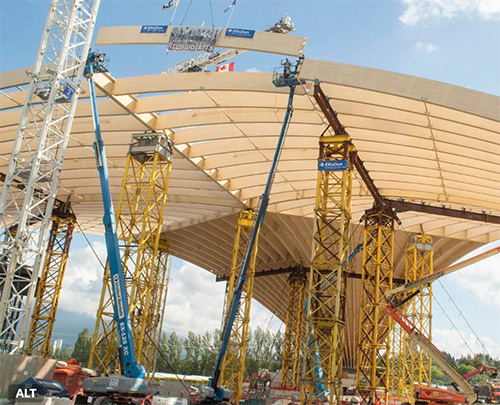 The Mobile Liberty Arch is under construction with cranes, temporary support towers and wooden roof arches being erected above.