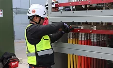 Worker installs large electrical power cables and switchgear equipment at a construction site.