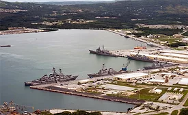 Aerial view of Naval Base Guam waterfront facilities and Navy ships docked at piers.