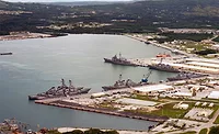 Aerial view of Naval Base Guam waterfront facilities and Navy ships docked at piers.