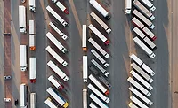 Aerial view of dozens of commercial trucks and trailers parked in organized rows at a large freight parking facility.
