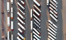 Aerial view of dozens of commercial trucks and trailers parked in organized rows at a large freight parking facility.