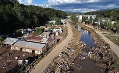 Aerial view of flood damage in western North Carolina following Hurricane Helene, showing debris-lined waterways, damaged buildings and washed-out infrastructure.