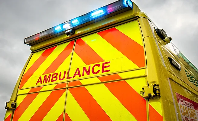 Photo shows the back of an ambulance with alternating orange and yellow stripes and a bar of blue and red lights across the top