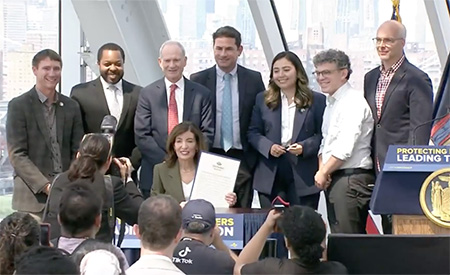 New York Gov. Kathy Hochul signs Executive Order No. 62 surrounded by lawmakers and supporters at a signing ceremony.