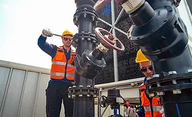 Workers install industrial piping and mechanical equipment at a construction site.
