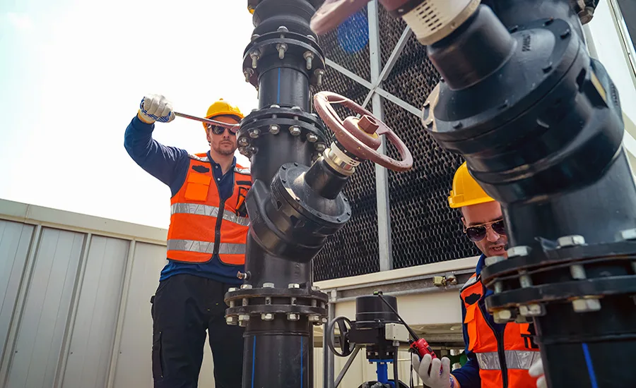 Workers install industrial piping and mechanical equipment at a construction site.