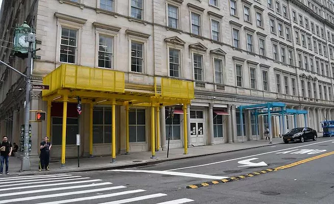 WEB NYC Scaffolding Sheds Photo shows new sidewalk shed designs along a street in New York City; one is yellow, the other blue
