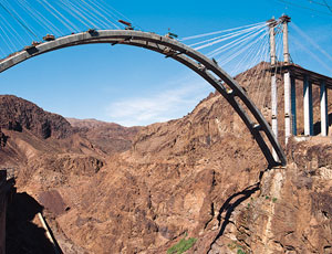 Contractor excavated to sheer drops on either side of Black Canyon for foundations. Temporary cable stays hold the arch in place during construction, now scheduled to finish next year.