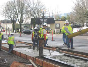 After laying form work, workers pour concrete to embed the track (this image) which will eventually take the look of this artist’s rendering of the intersection at Grand Ave. and Stark St. (below). The streetcar is growing in popularity across the country, in part because no vehicle traffic lanes are lost and the construction is less expensive than light rail.