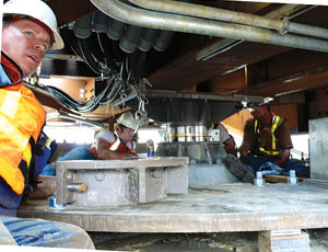 Crane operator holds span over pivot assembly while workers install collar.