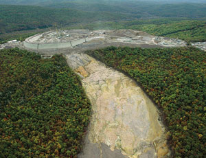 Roller-compacted concrete dam (below) will replace earth-and-rockfill dam that failed, clearing forest from the mountainside.